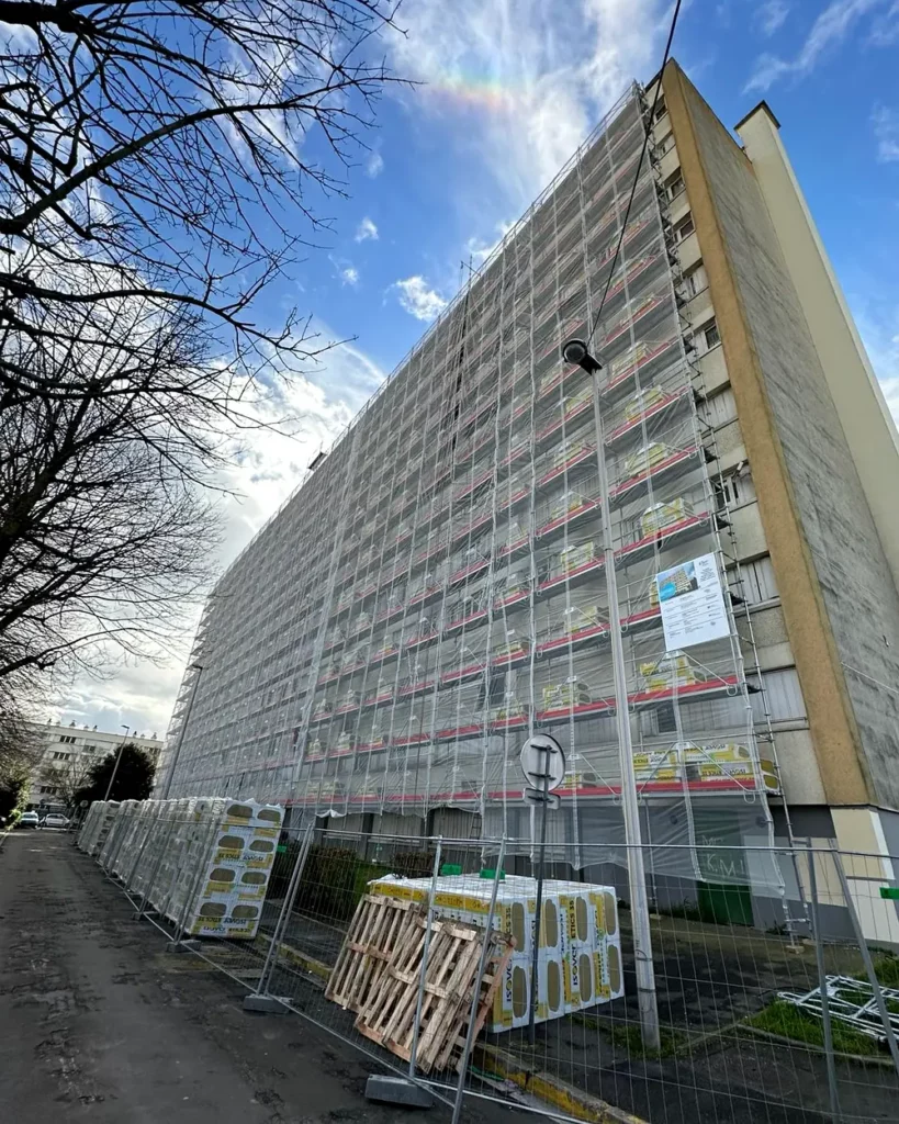 Façade complète d'un immeuble de logements sous échafaudage de ravalement, filets de protection et plateaux de travail sur toute la hauteur