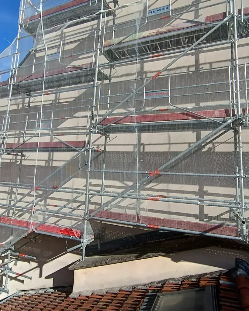 Échafaudage de ravalement monté depuis la toiture d'un immeuble ancien, en rue étroite
