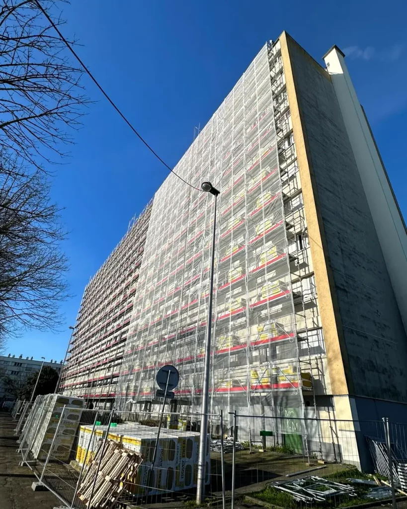 Échafaudage de façade monté par Matrix Service sur un immeuble de logements, palettes d'isolant au pied du bâtiment pour une isolation thermique par l'extérieur